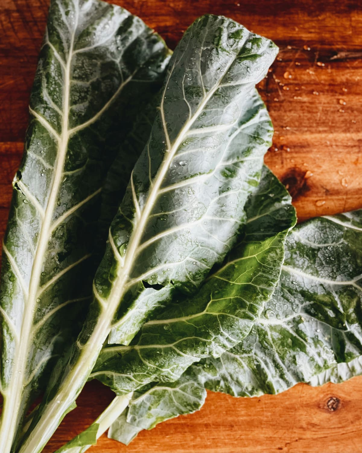 Fresh collard green leaves with prominent white veins on a wooden cutting board